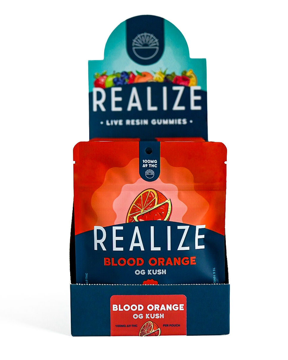 Wholesale display box featuring Realize Live Resin Gummies in Blood Orange OG Kush flavor. The display contains bright orange 100mg Δ9 THC gummy pouches with a blood orange illustration and Realize branding, presented in a navy countertop display with a matching Blood Orange OG Kush product label.